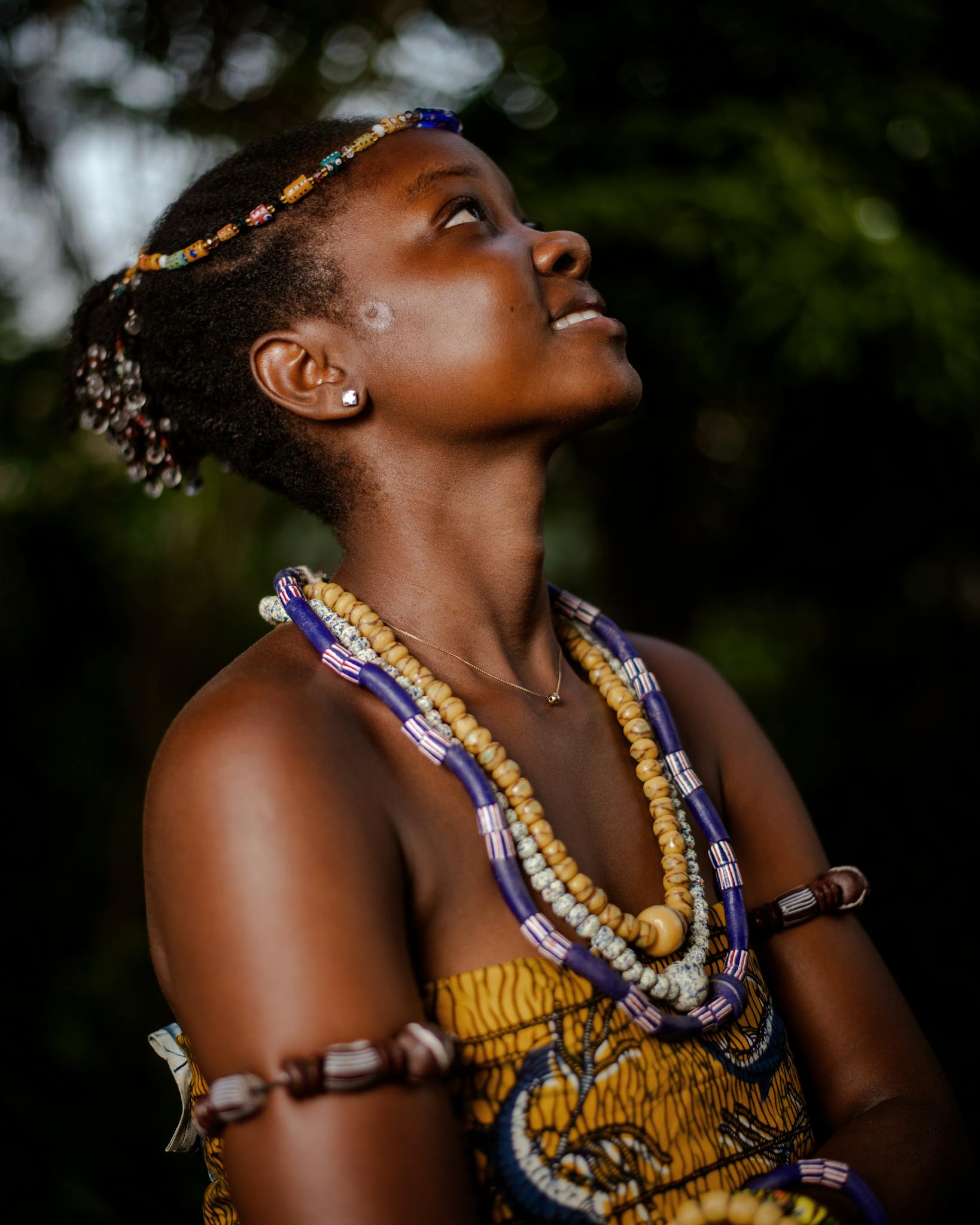 A young African woman proudly wearing traditional jewelry, posing outdoors.